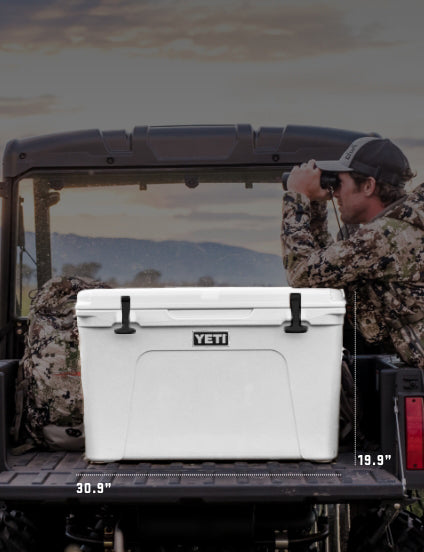 White YETI cooler in the back of a truck with a person in camouflage gear looking through binoculars.