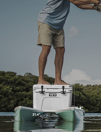 Person standing on a YETI cooler in the water with trees in the background