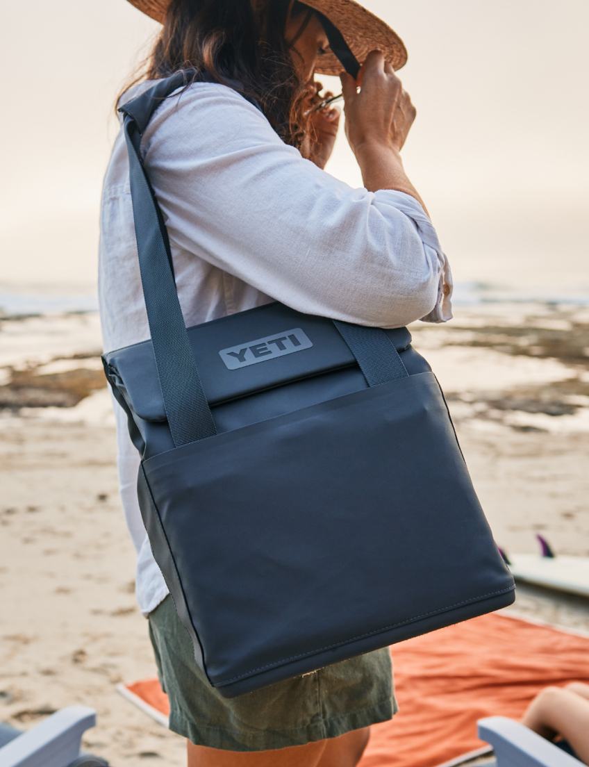 Person holding a YETI cooler bag on a beach