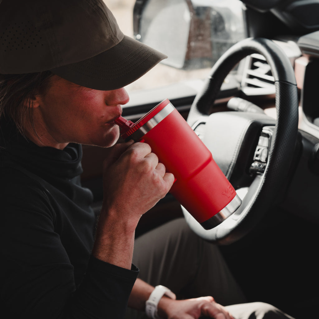 Person sitting in a car, drinking from a red insulated Rambler Travel Straw Mug.