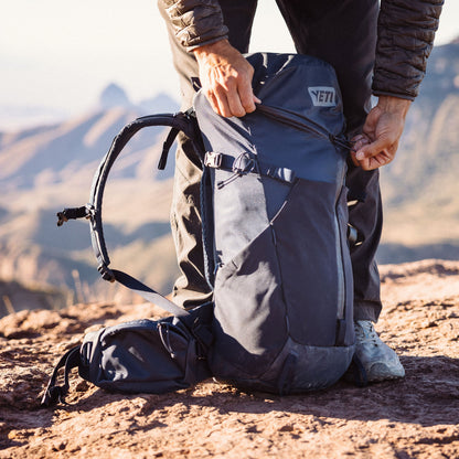 Person adjusting a backpack with a mountainous landscape in the background