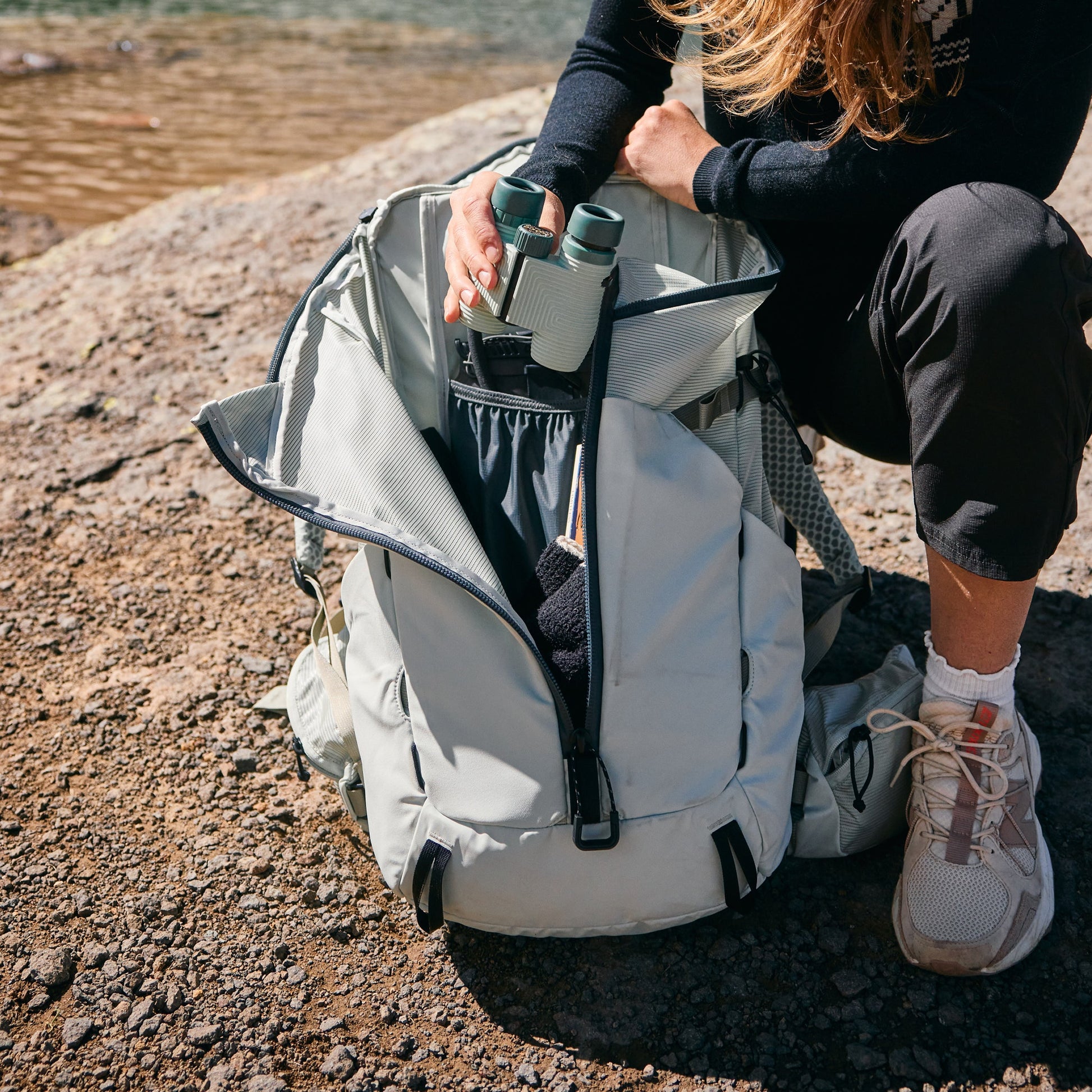 Person sitting on a rocky surface with a backpack and binoculars.