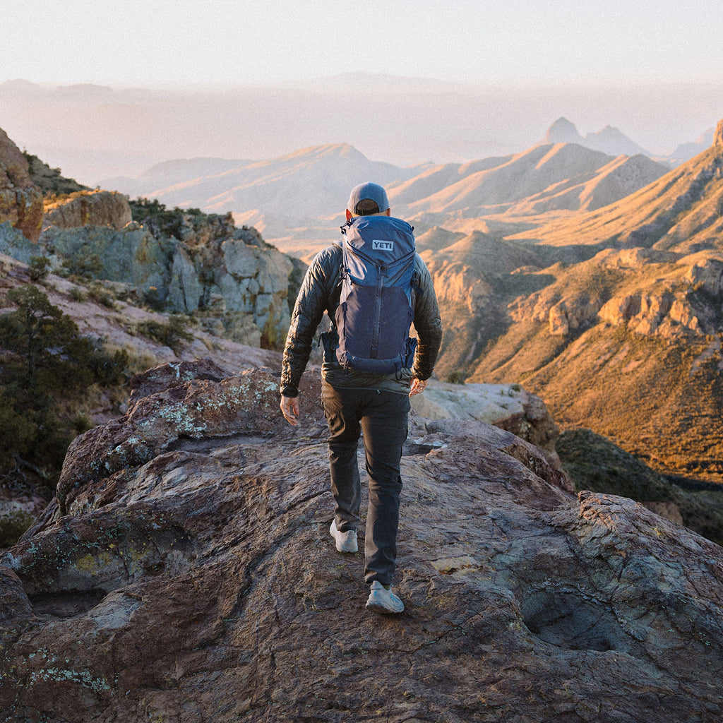 Person with a backpack walking on a rocky mountain trail with scenic views.