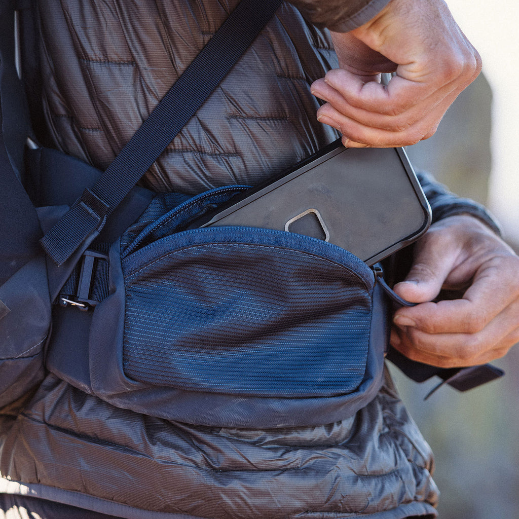 Person holding a smartphone with a blue bag over their shoulder