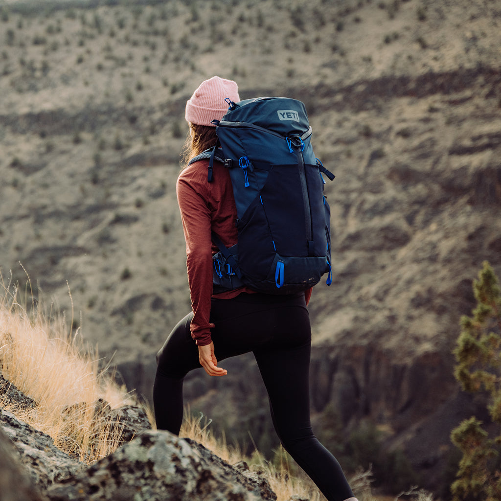 Person hiking with a navy YETI backpack in a mountainous landscape