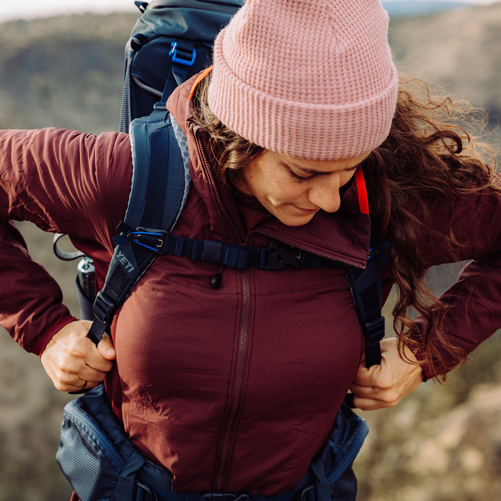 Person wearing a maroon jacket and pink beanie with a backpack outdoors