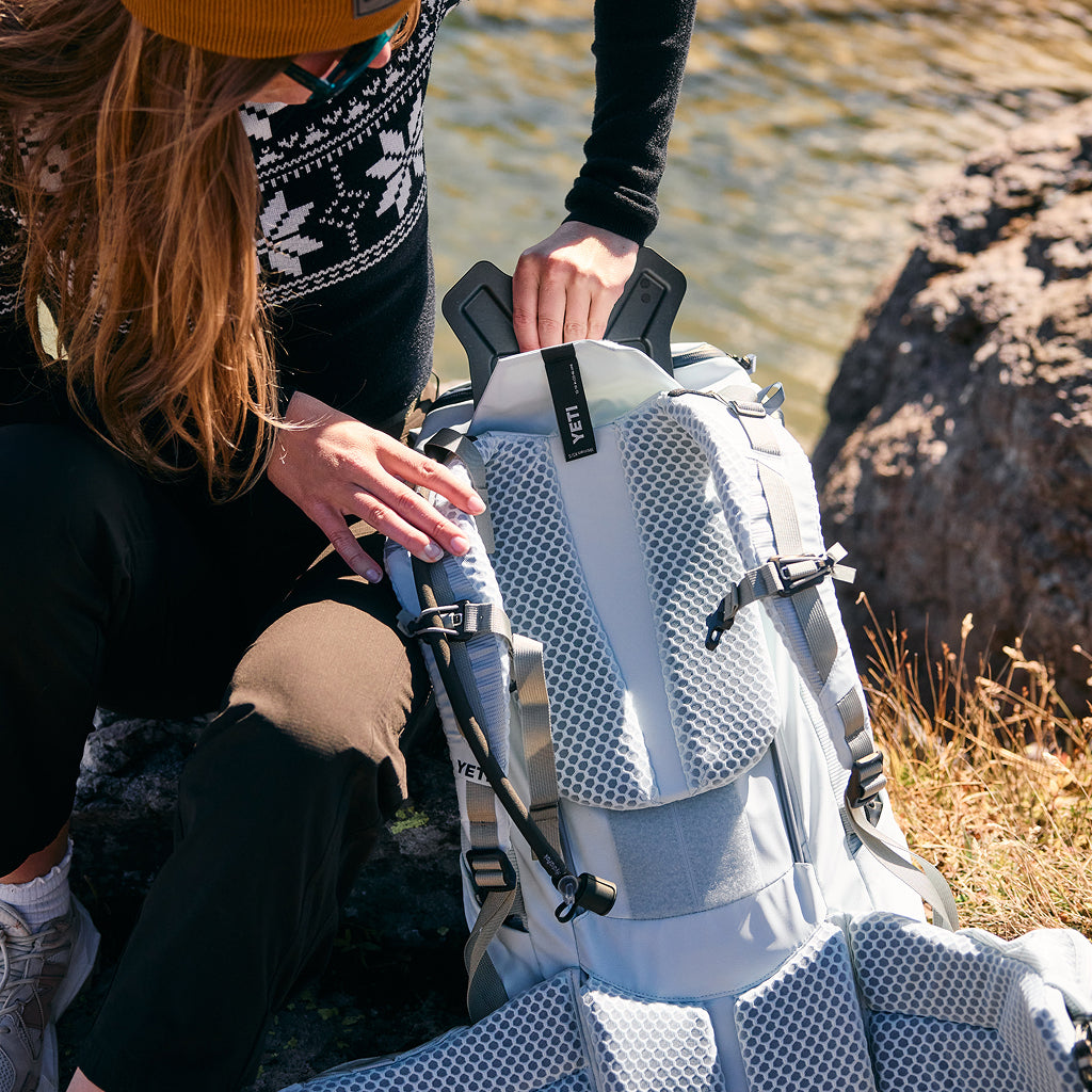 Person sitting by a body of water with a white backpack featuring a brand logo.