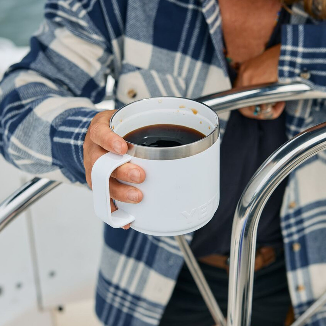 Person holding a white mug with coffee on a boat