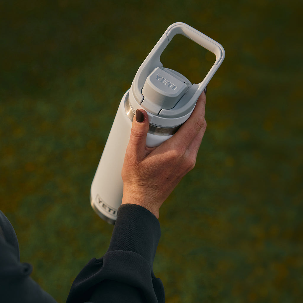 Hand holding a white YETI water bottle against a blurred natural background