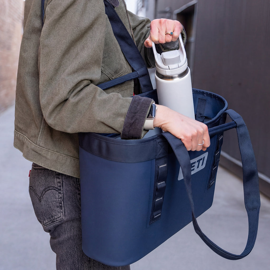 Person holding a blue bag with a white water bottle, standing next to a vehicle.