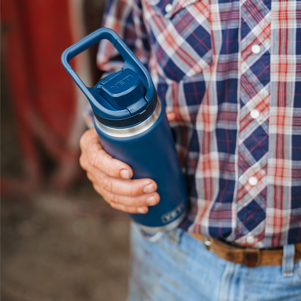 Person holding a blue insulated water bottle with a person wearing a plaid shirt in the background