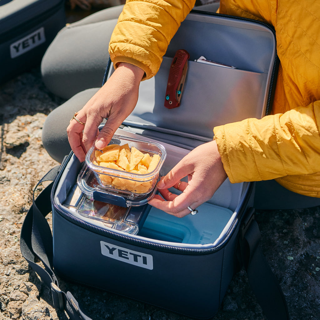 Person opening a YETI cooler with a container of snacks
