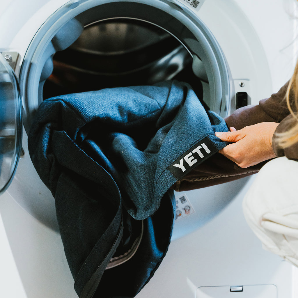 Person placing a blue YETI dog bed cover into a washing machine.