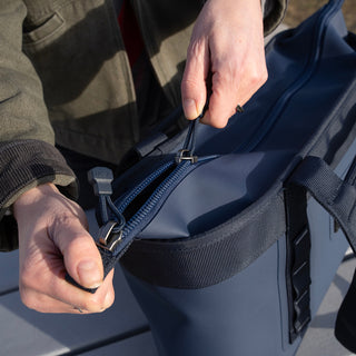 Person zipping a navy blue YETI  bag on a vehicle