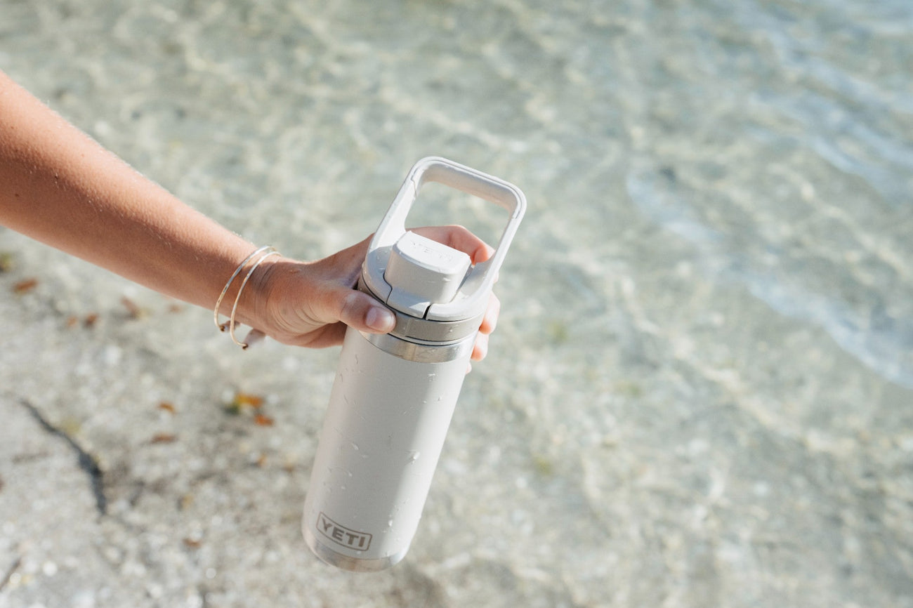 Person holding a white Yeti water bottle by a body of water