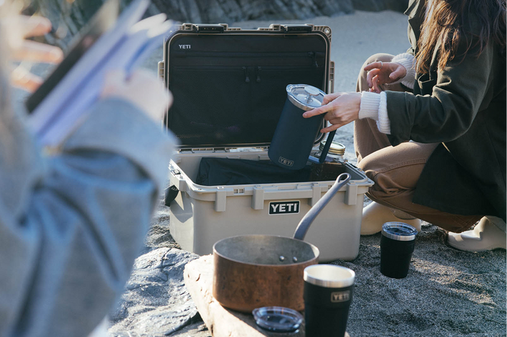 People around a YETI cooler with camping gear on a rocky surface