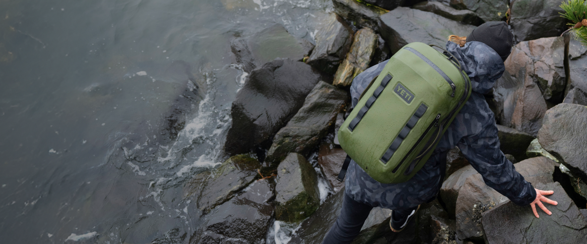 Person with a green backpack crossing a rocky stream