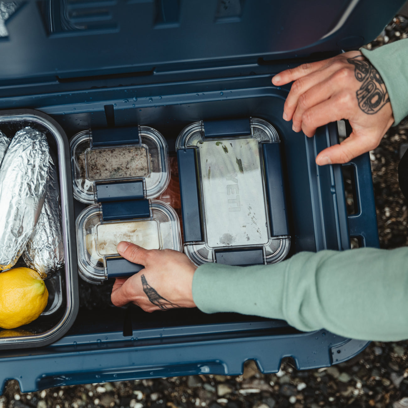 Person organizing food containers in a blue cooler outdoors