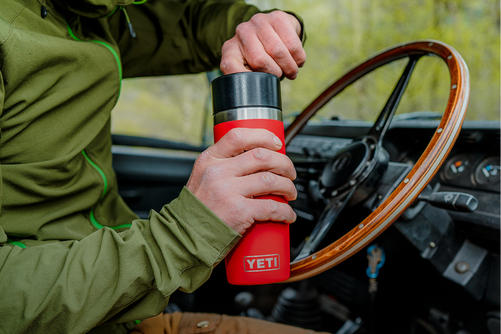 Person holding a red YETI mug inside a vehicle